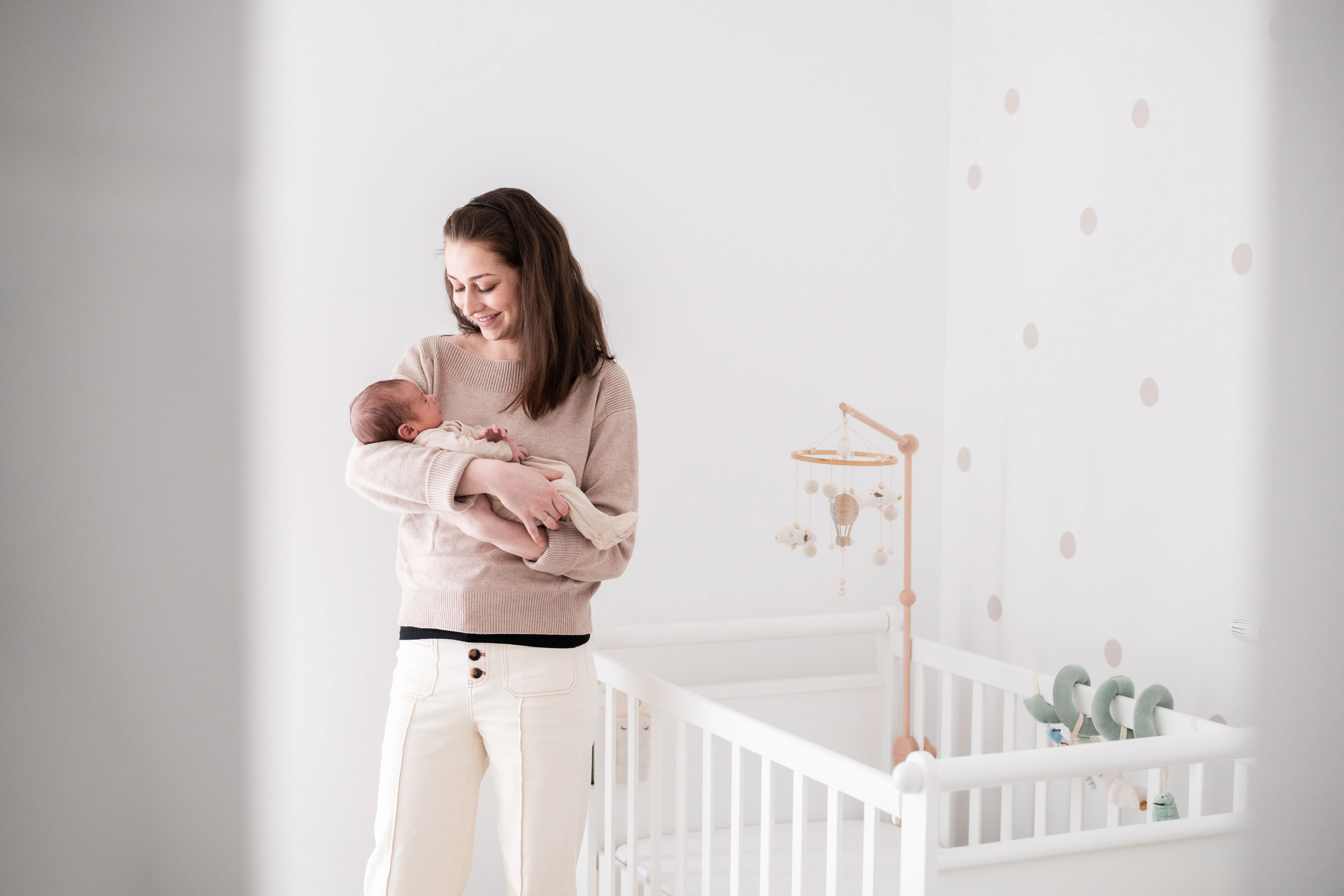 Photo d'une maman tenant son nouveau-né dans les bras, dans la chambre de bébé à côté de son petit lit à Avon, à côté de Fontainebleau