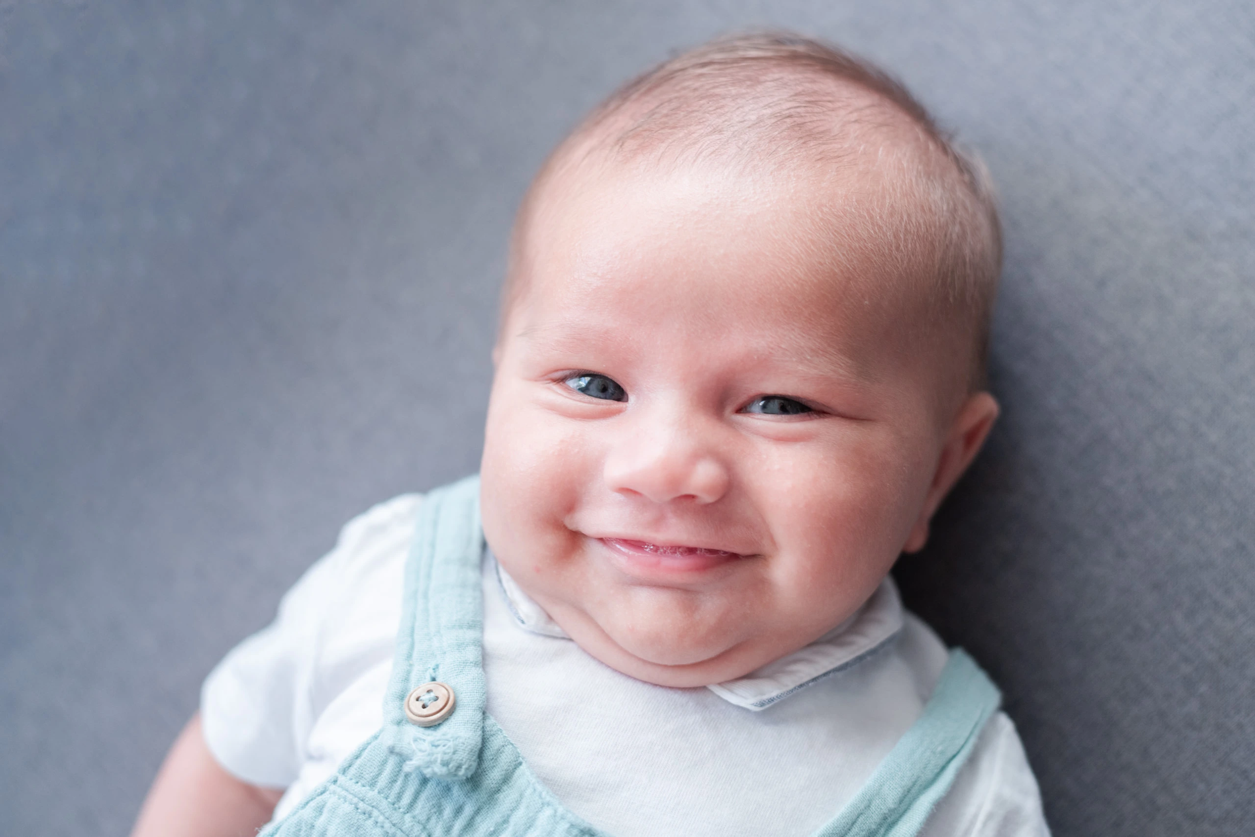 Portrait d'un bébé allongé qui sourit, lors d'une séance photo famille avec bébé réalisée à domicile près de Fontainebleau en Seine et Marne