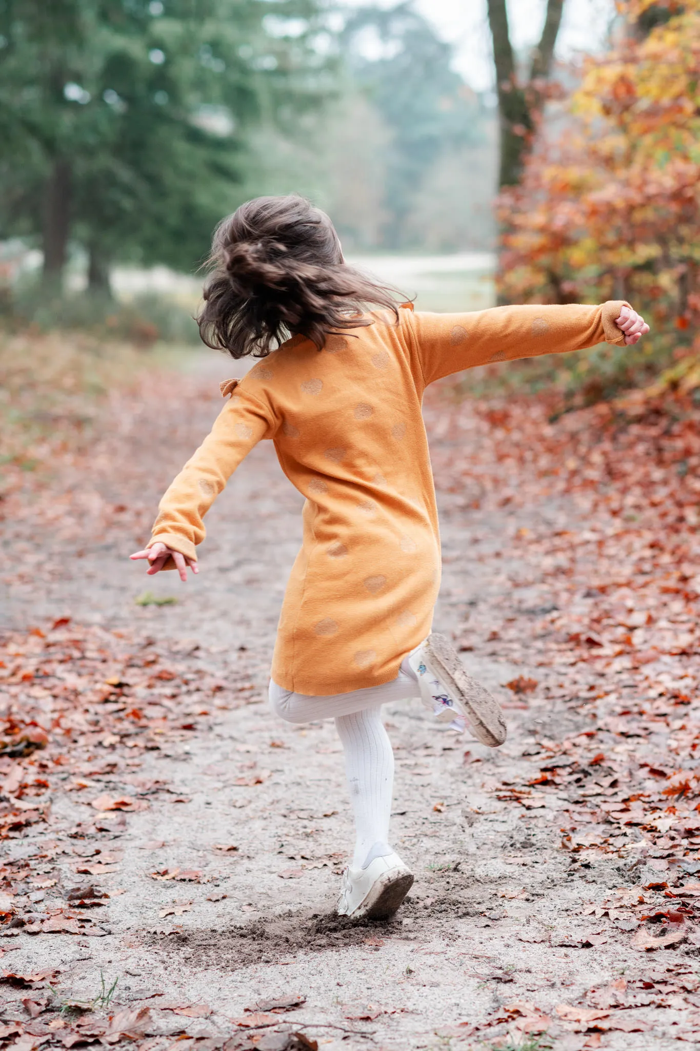 Enfant de dos, qui fait un tour sur elle-même et qui danse lors d'une séance photo en famille en forêt de Fontainebleau à l'automne