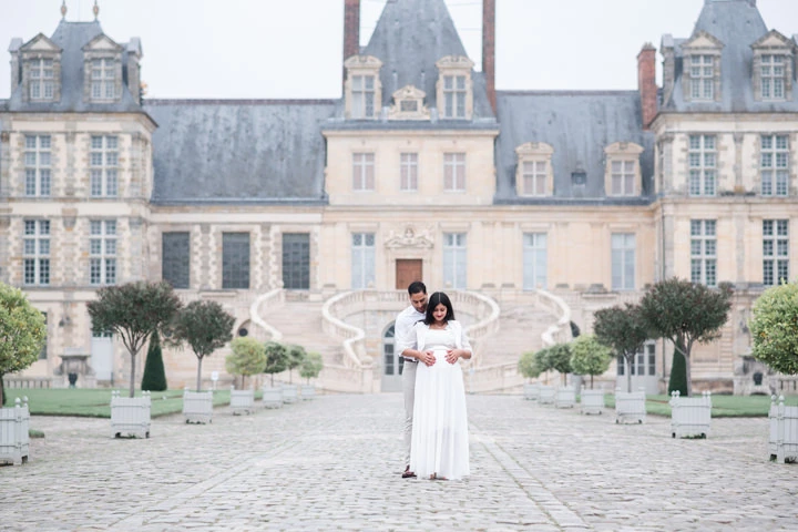 Femme enceinte et son mari, habillés en blanc, lors d'une séance photo de grossesse au Château de Fontainebleau