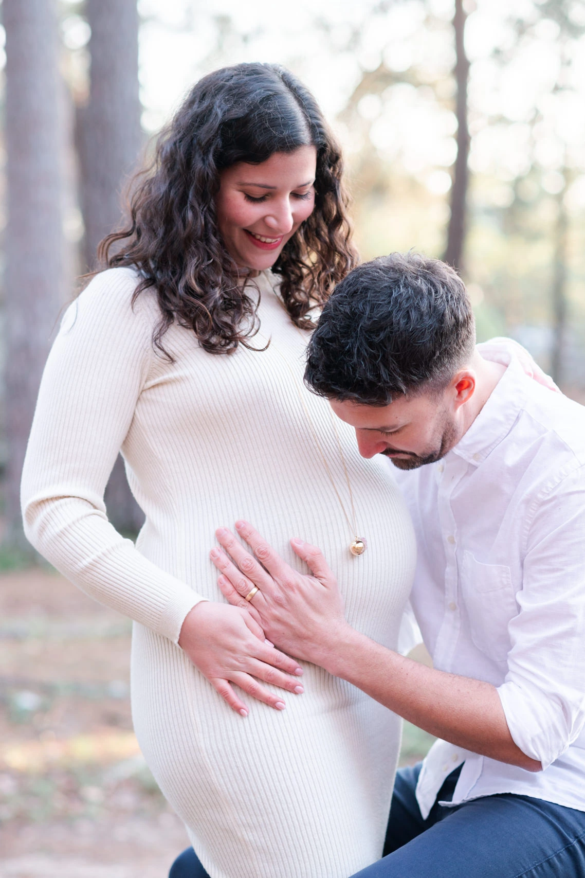 Femme enceinte et son mari, habillés en blanc, lors d'une séance photo de grossesse en forêt de Fontainebleau à l'automne