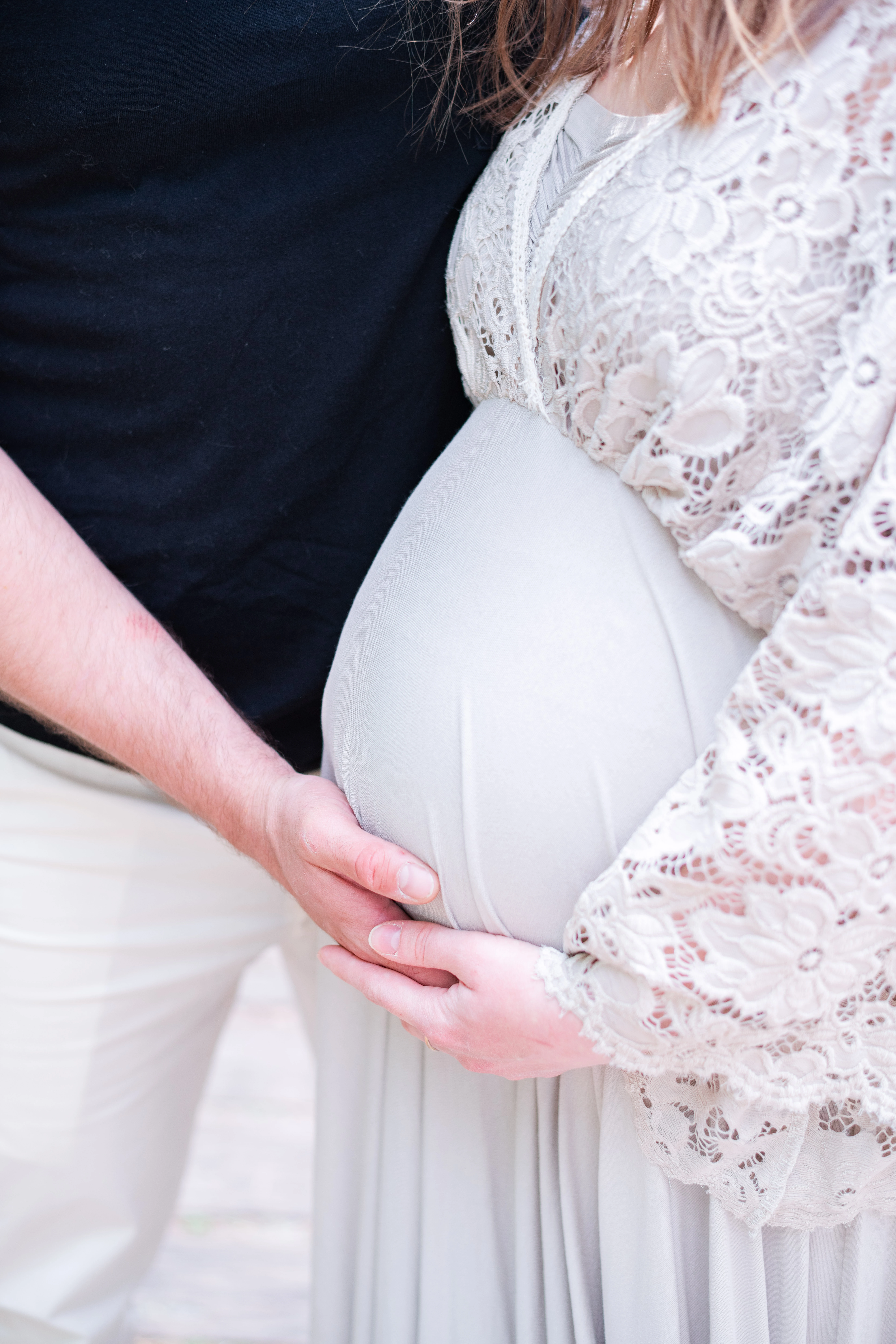 Ventre d'une femme enceinte, avec les mains des futurs parents apposées dessus, lors d'une séance photo grossesse près de Fontainebleau
