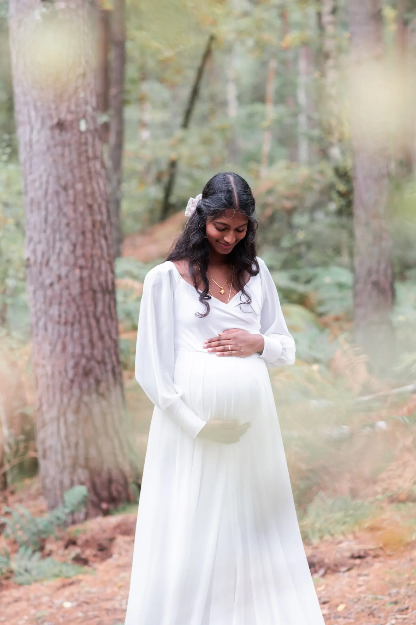 Femme enceinte, habillée en blanc, lors d'une séance photo de grossesse en forêt de Fontainebleau à l'automne