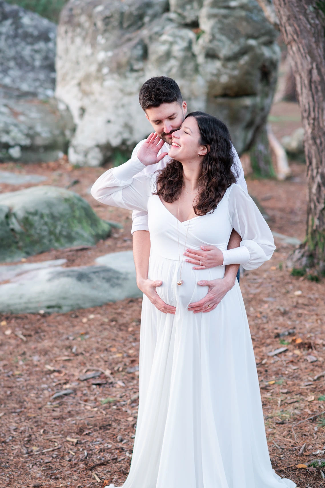 Femme enceinte et son mari, habillés en blanc, lors d'une séance photo de grossesse en forêt de Fontainebleau à l'automne