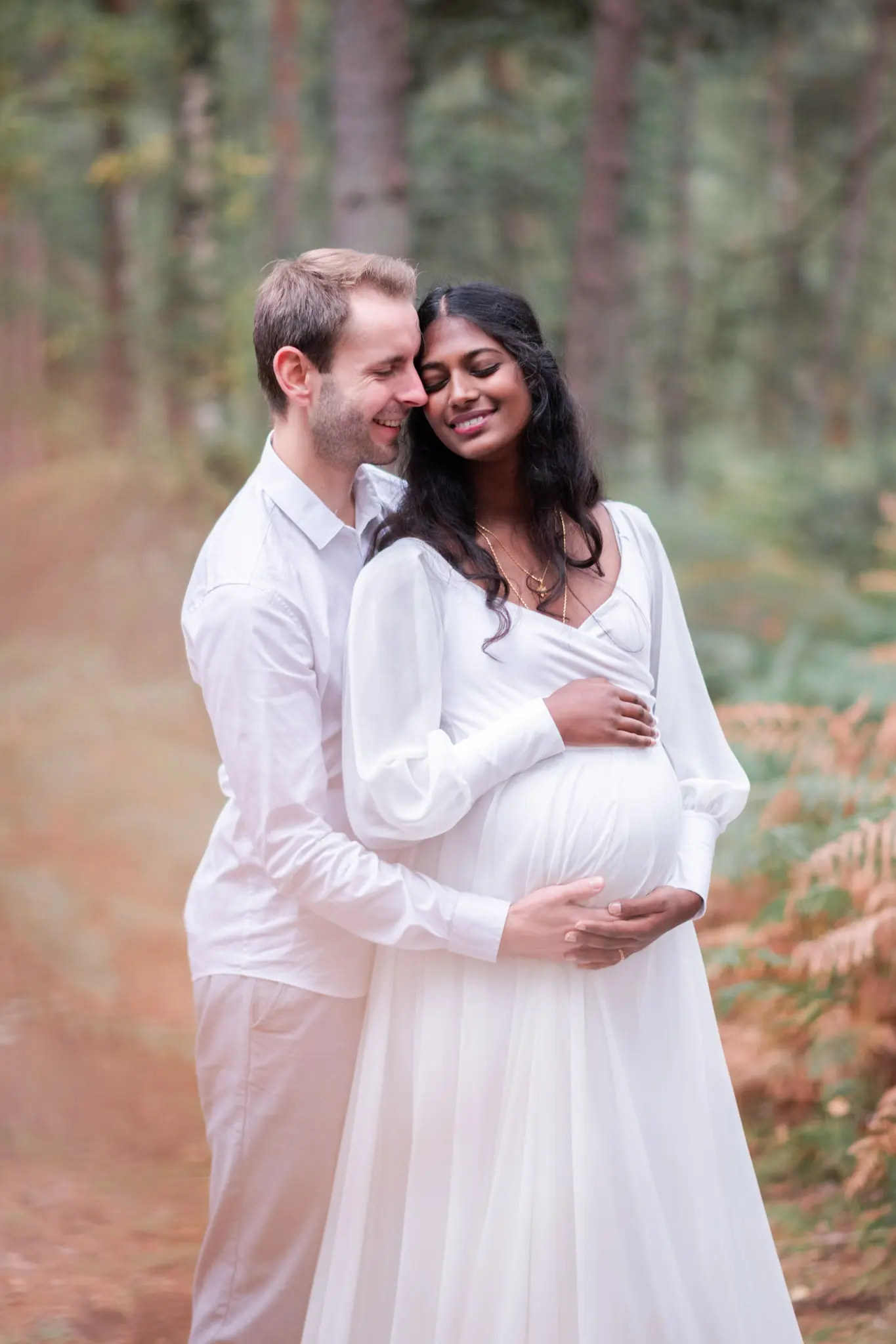 Femme enceinte et son mari, habillés en blanc, lors d'une séance photo de grossesse en forêt de Fontainebleau à l'automne