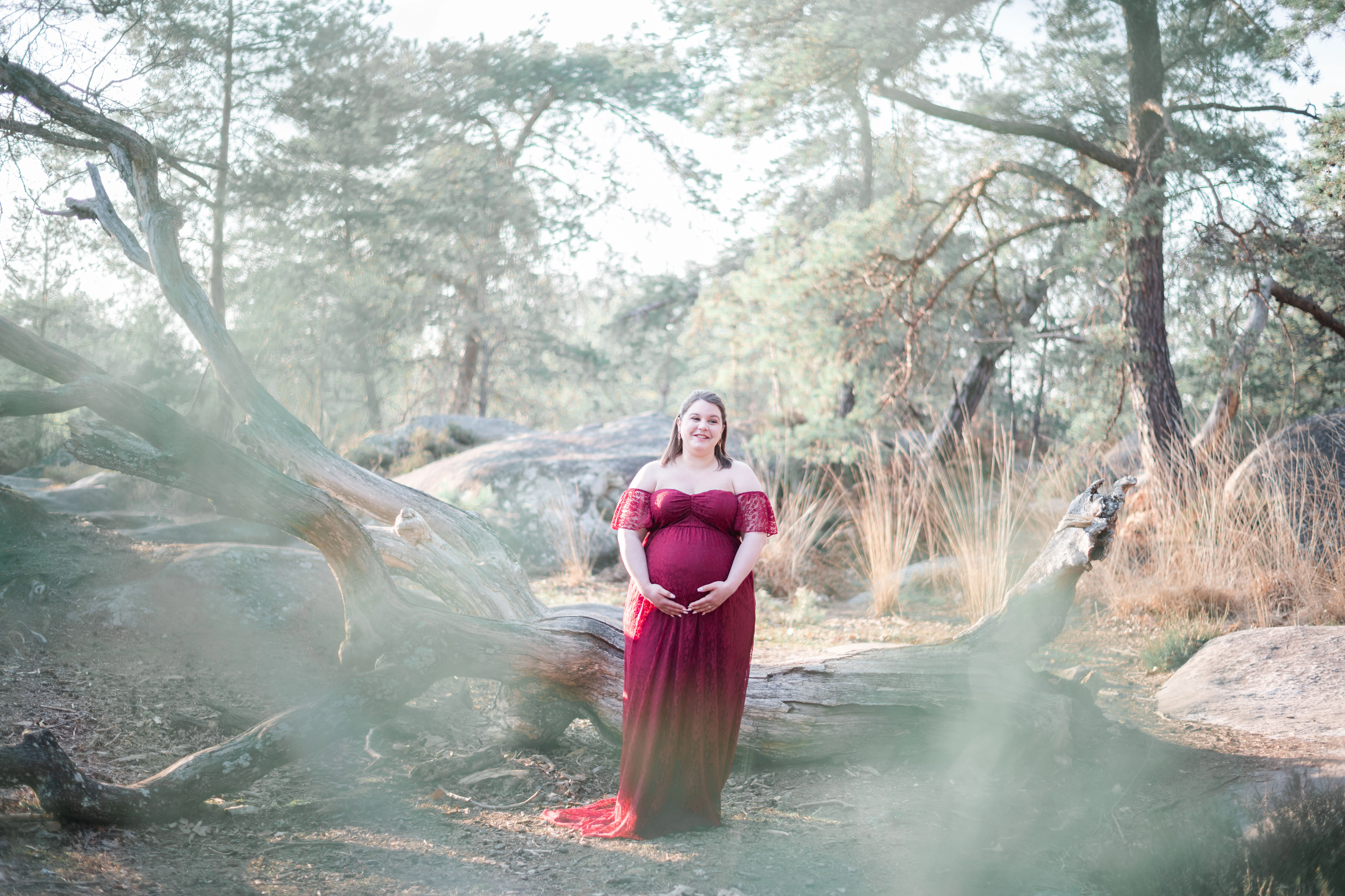 Femme enceinte dans une robe rouge bordeaux lors de sa séance photo grossesse en forêt de Fontainebleau