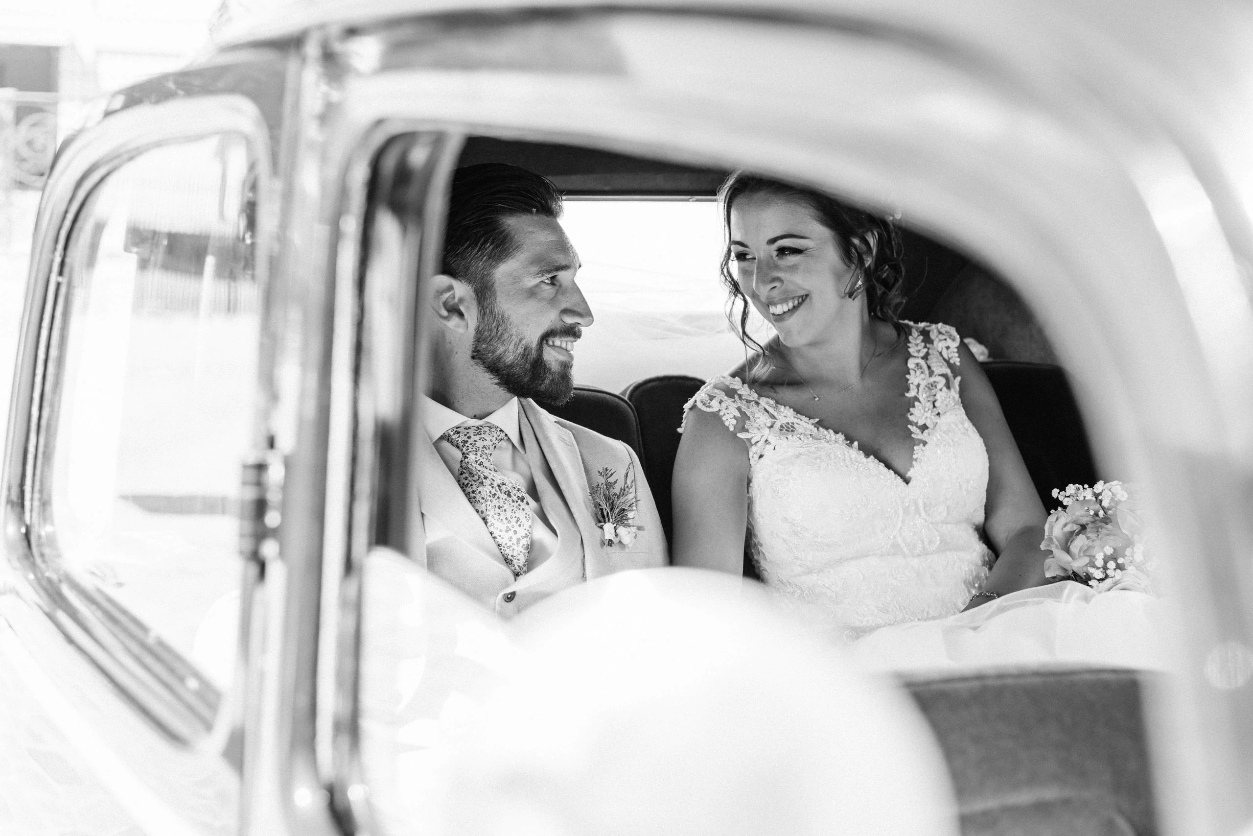Photo en noir et blanc d'un couple de mariés à Fontainebleau, dans une voiture ancienne