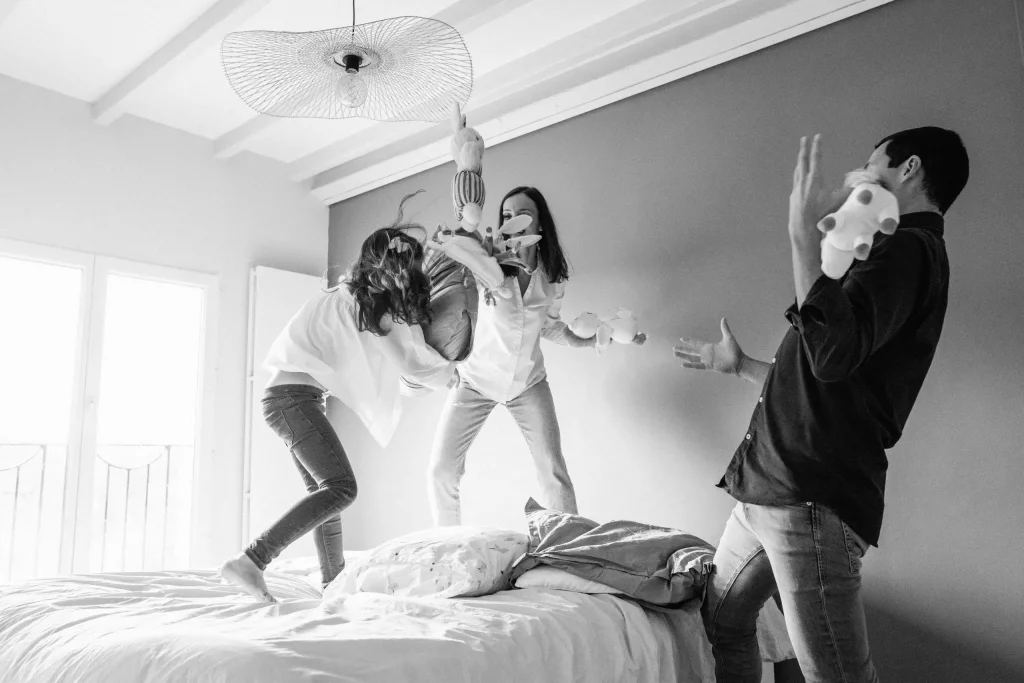 Famille en train de faire une bataille d'oreillers dans la chambre parentale lors d'une séance photo en famille
