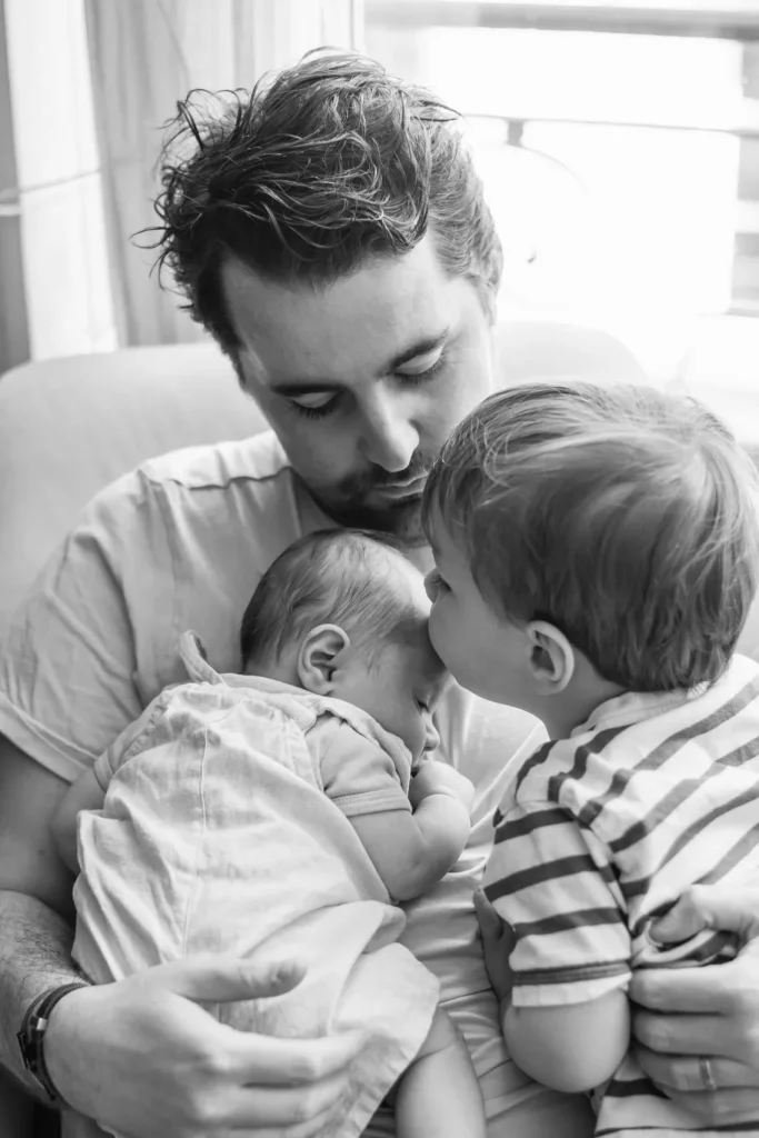 Moment de douceur et câlin en famille entre un papa et ses deux fils lors d'une séance photo en famille à leur domicile à Paris
