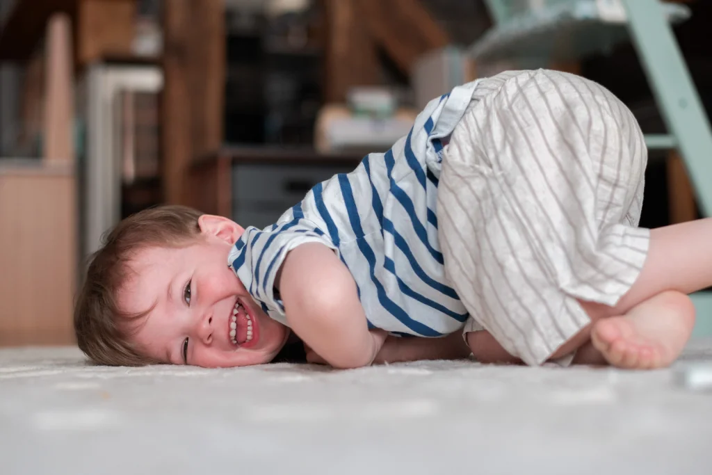 Enfant rigolant par terre dans son salon lors d'une séance photo à domicile à Fontainebleau