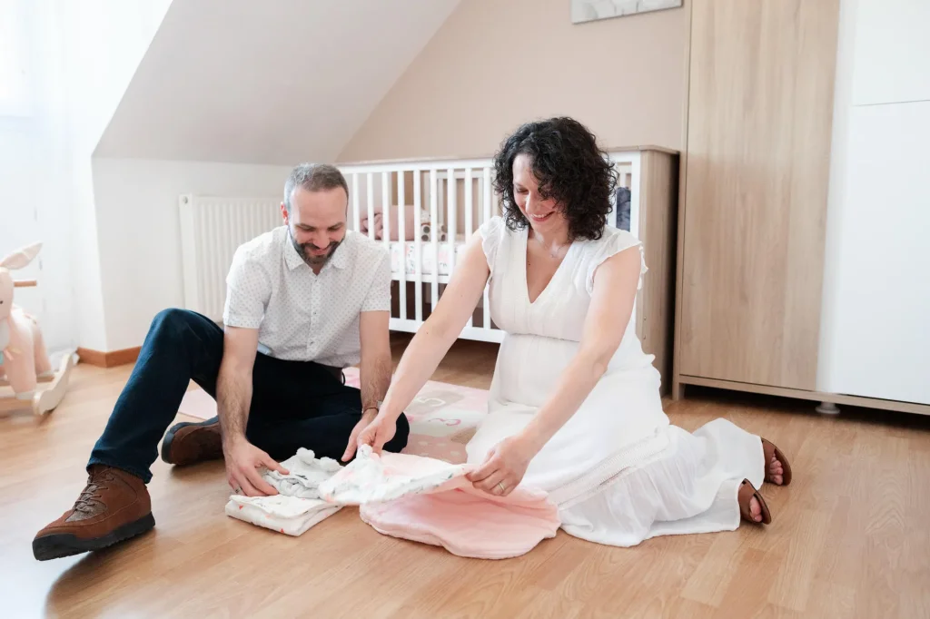 Futurs parents qui préparent les vêtements de leur futur bébé dans la chambre de l'enfant lors de leur séance photo de grossesse à domicile à Fontainebleau
