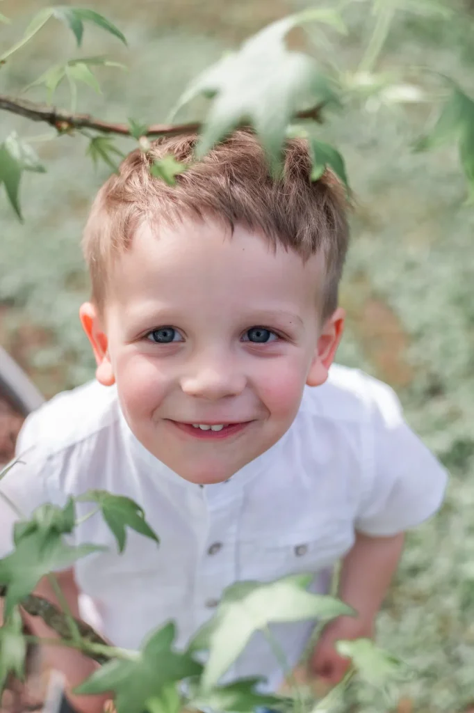 Enfant qui joue dans le jardin, entre les feuilles des arbres, lors d'une séance photo à domicile