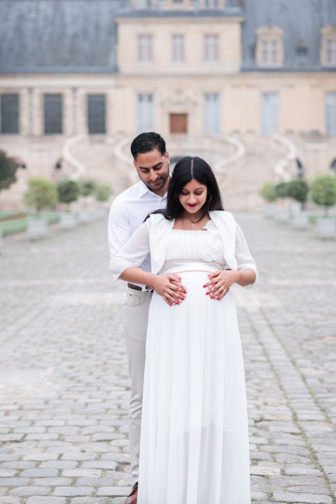 Couple habillé en blanc lors d'une séance photo grossesse dans la cour d'honneur du château de fontainebleau