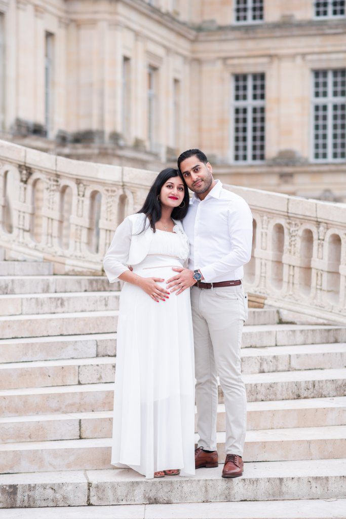 Couple avec femme enceinte lors de leur shooting grossesse, sur l'escalier du fer à cheval dans la cour d'honneur du château de fontainebleau