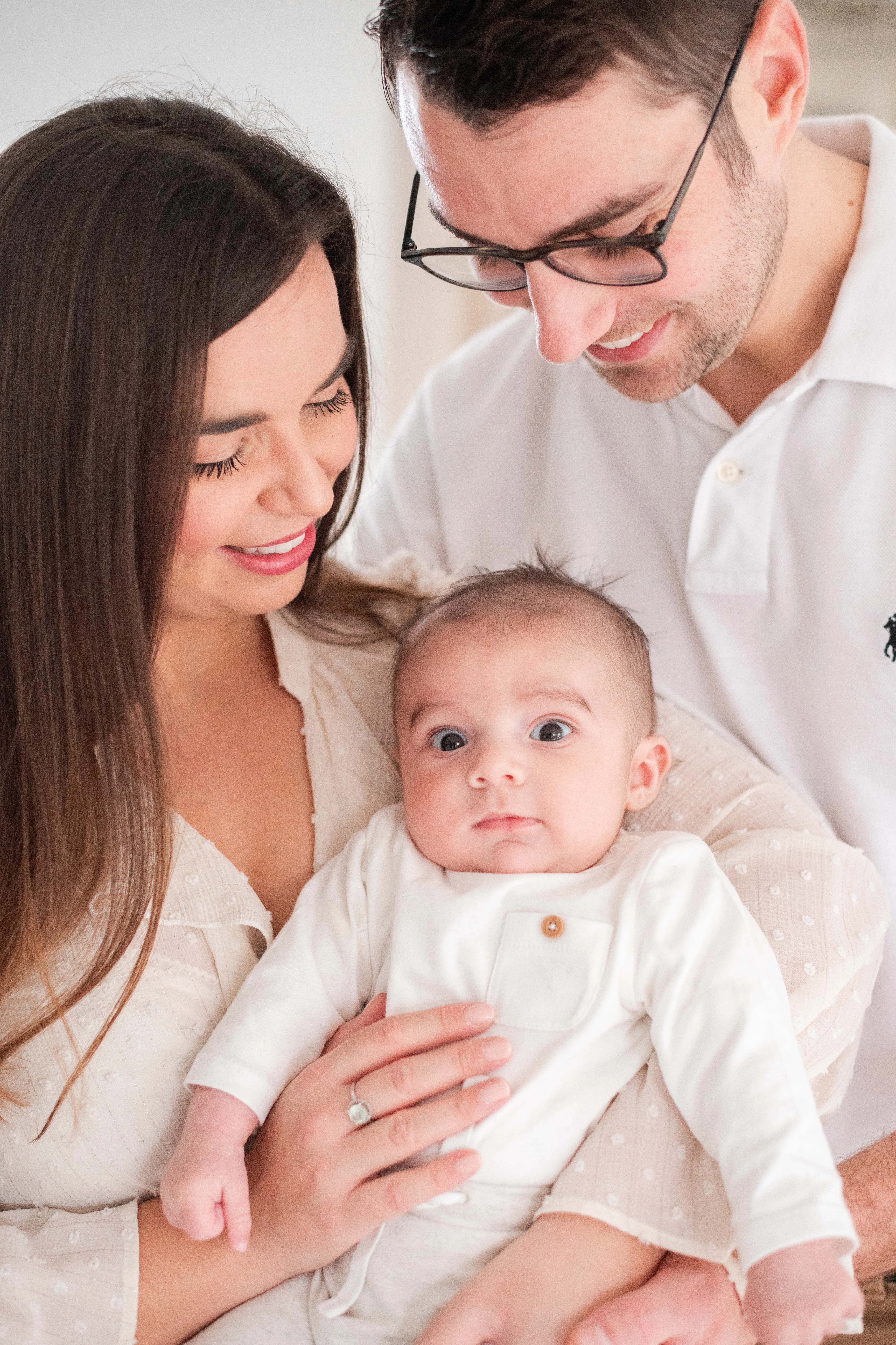 Portrait d'un bébé dans les bras de ses parents, écarquillant grand les yeux, lors d'une séance photo avec un photographe professionnel près de Melun