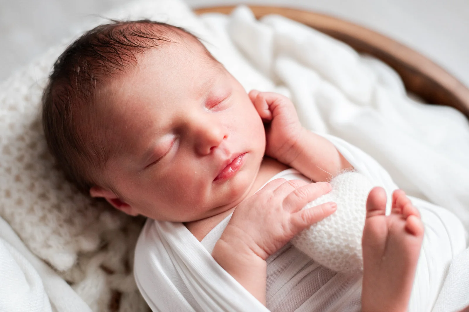 Gros plan sur le visage d'un nouveau-né emmailloté, tenant un petit doudou en forme de coeur, lors de sa séance photo de naissance à domicile près de Melun