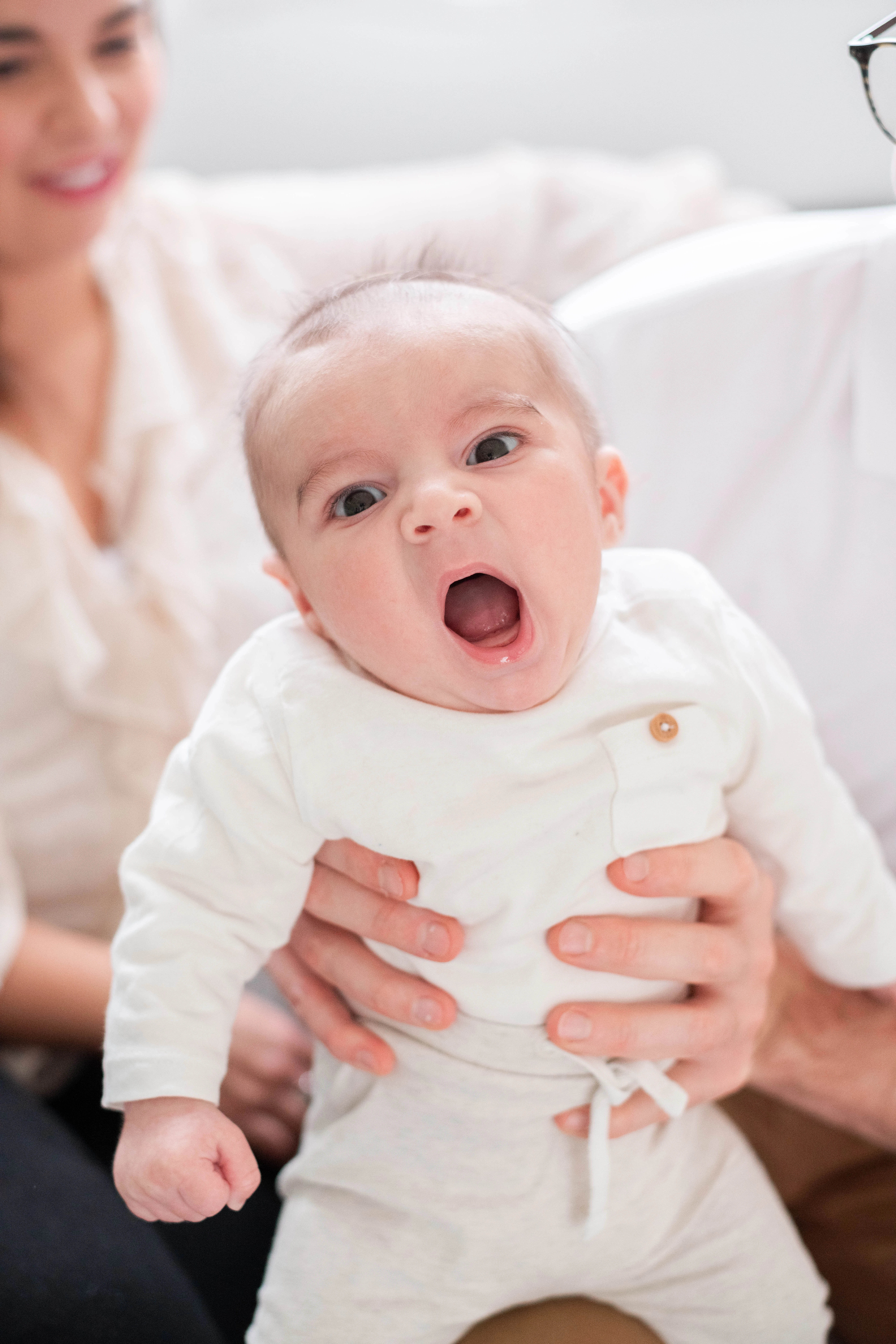 Photo d'un bébé sur les genoux de ses parents lors d'une séance photo à domicile près de Melun, en train de bailler